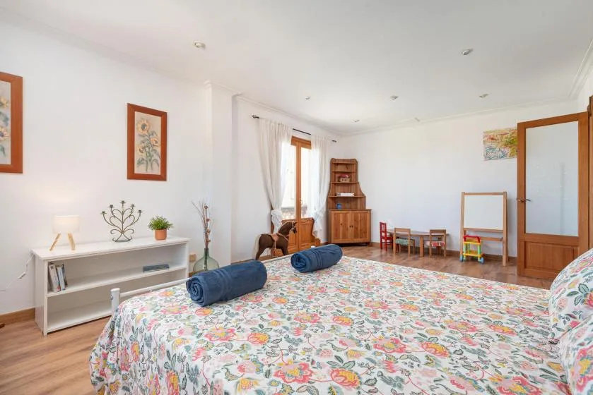 A bright bedroom features a floral bedspread and a small seating area by the window.