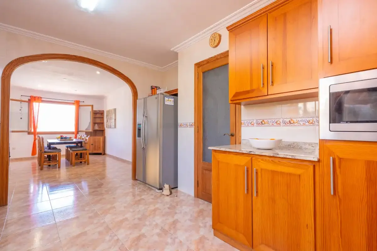 A kitchen with wooden cabinets opens through an archway to a dining area.