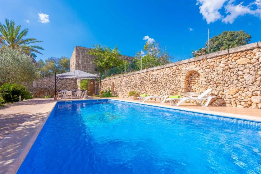 An outdoor swimming pool sits beside a stone wall and shaded seating area.