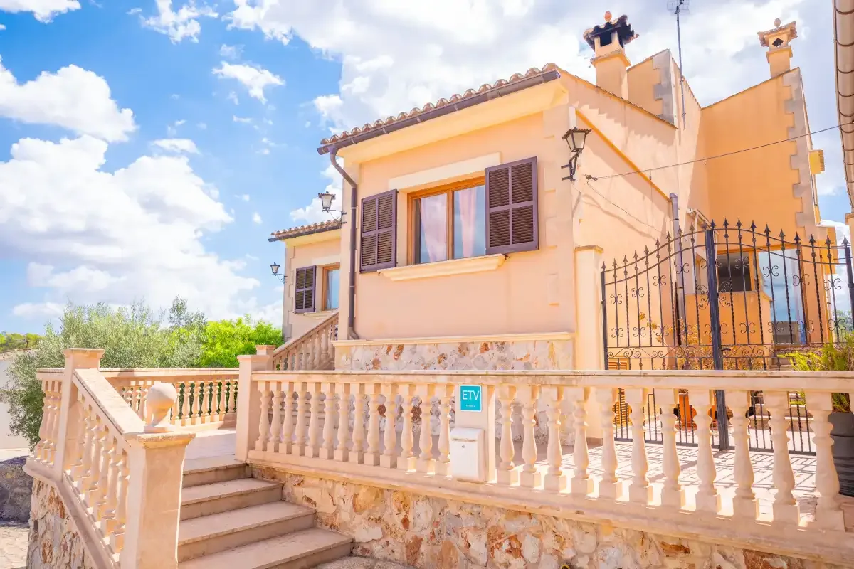 A peach-colored house stands behind a stone balustrade and exterior steps.