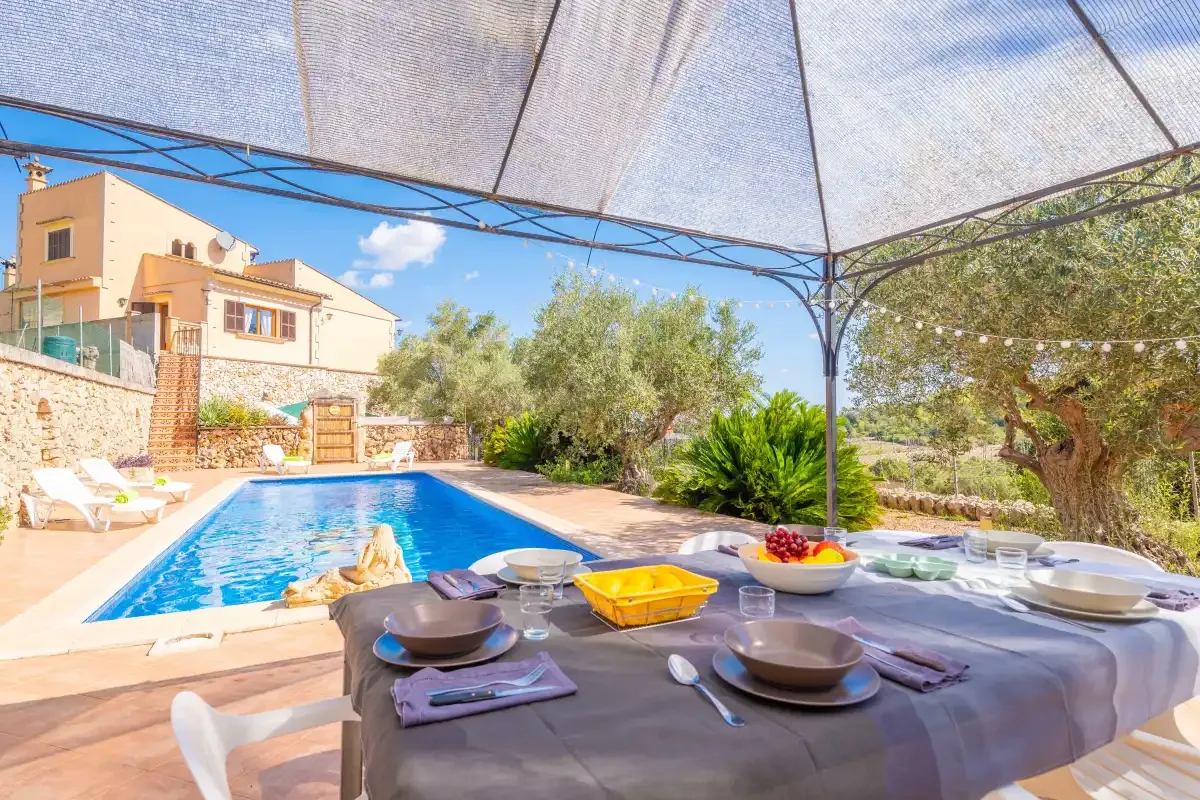 An outdoor dining table sits beside a swimming pool under a shade canopy.
