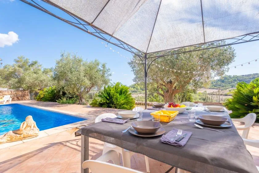Outdoor dining area beside a swimming pool, shaded by a large canopy.