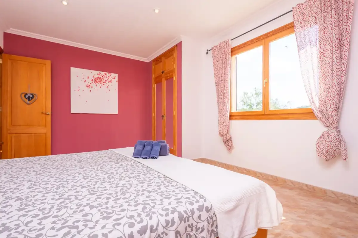 A bedroom with a patterned bedspread and a window with pink curtains.