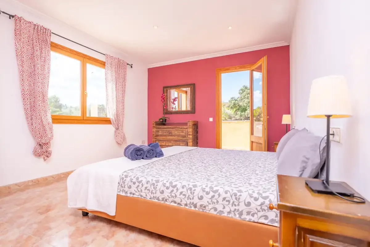 A bedroom with a patterned bedspread, wooden dresser, and open balcony door.