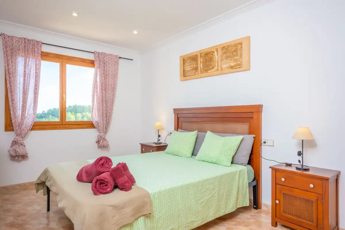 A bedroom with a wooden bed, green bedding, and a window with curtains.