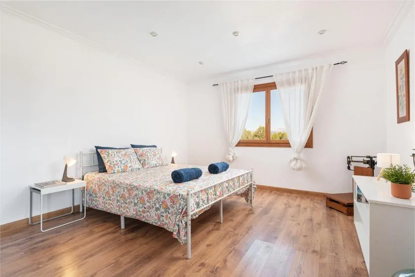 A bright bedroom with a patterned bed and a window framed by white curtains.