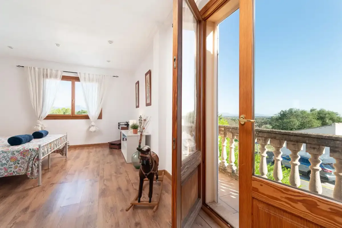 A bright room with a bed and an open door leading to a balcony.