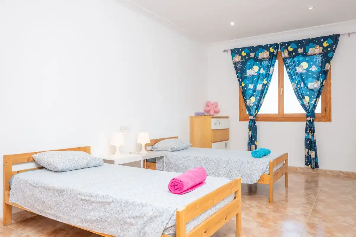 A bright bedroom with two single beds and blue patterned curtains.