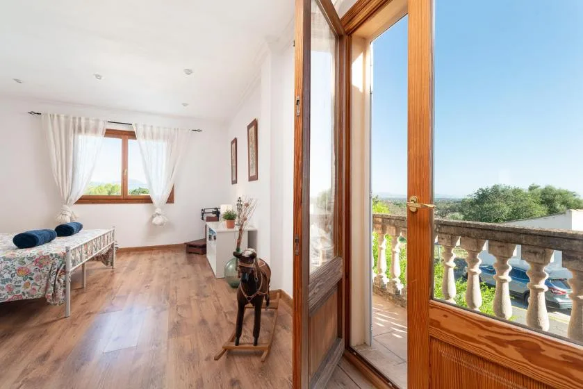A bright room with a bed and an open wooden door onto a balcony.
