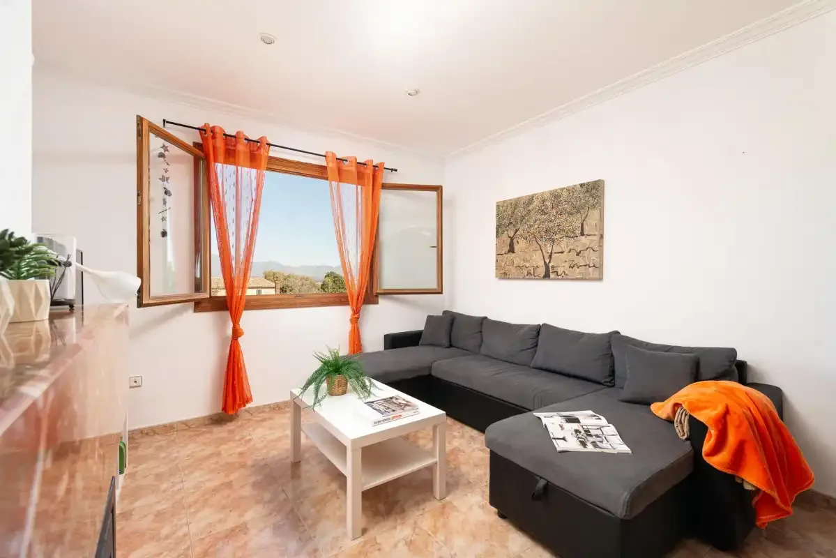 A living room with a dark sectional sofa and orange curtains by the window.