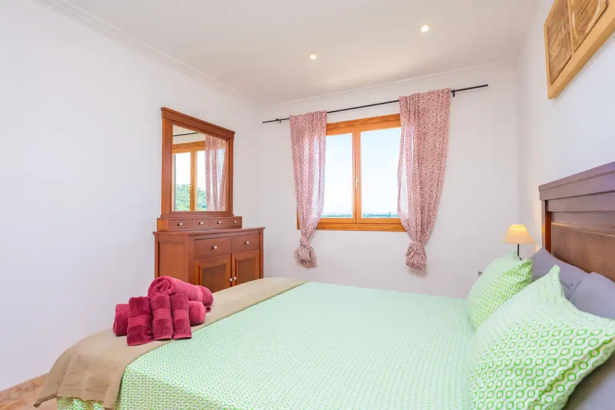 A bedroom with a mint-green bed and a wooden dresser beneath a window.