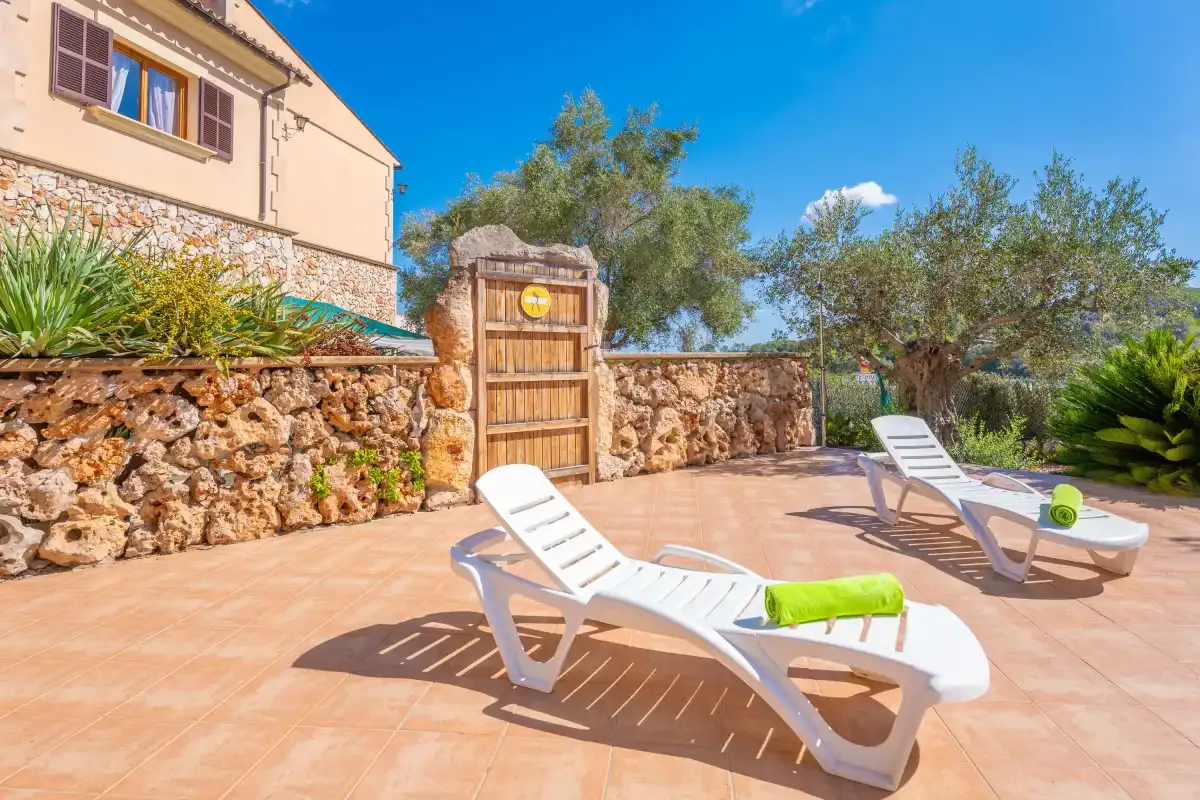 A sunny outdoor patio with reclining loungers beside a stone wall.