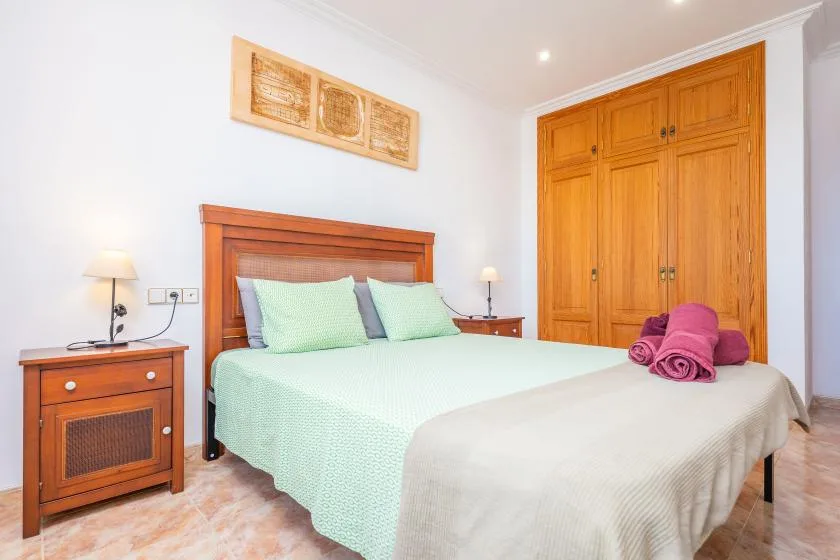 A bedroom with a bed, bedside tables, and a wooden wardrobe.