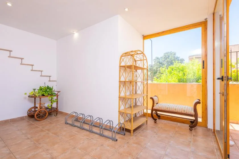 A bright interior opens onto a sunny balcony, with a bench and shelving nearby.