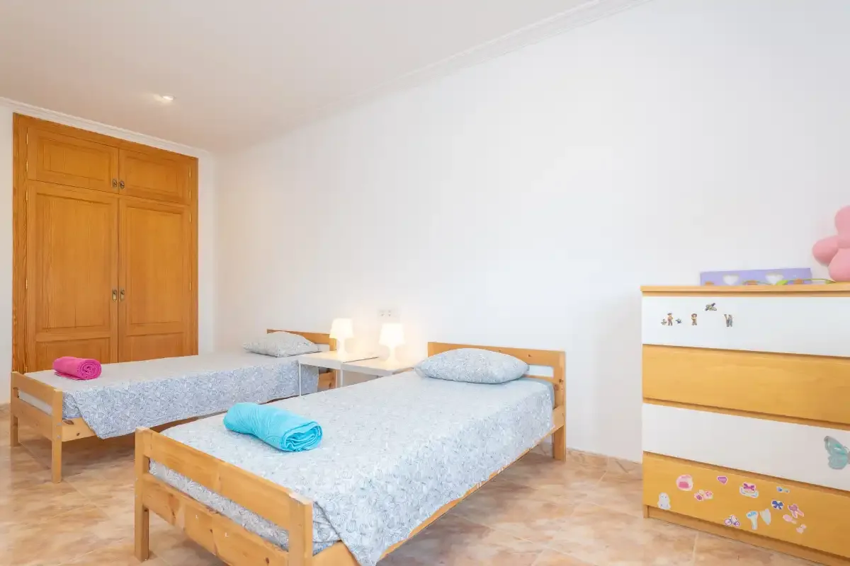 A bright bedroom with two single beds and a wooden dresser.