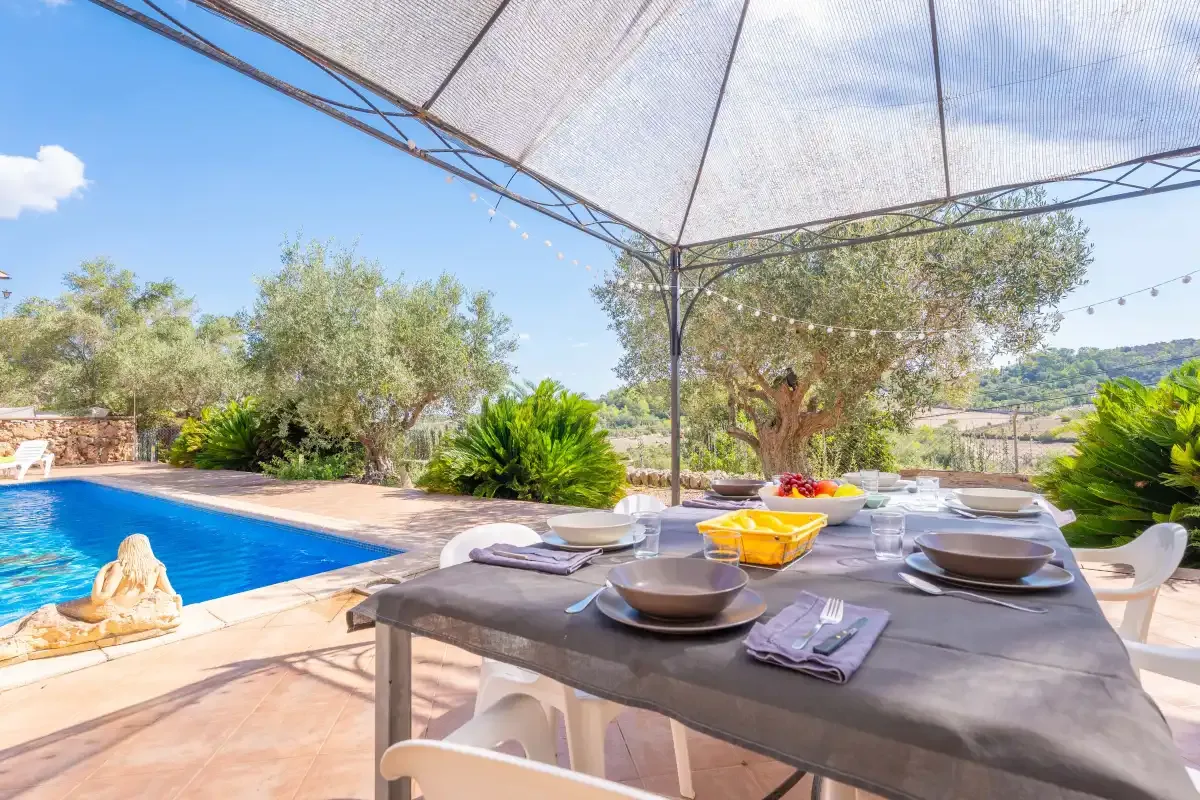 An outdoor dining table beside a swimming pool, with a large shade canopy overhead.