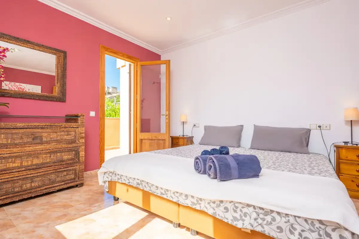 A bedroom with a double bed, wooden dresser, and open balcony door.