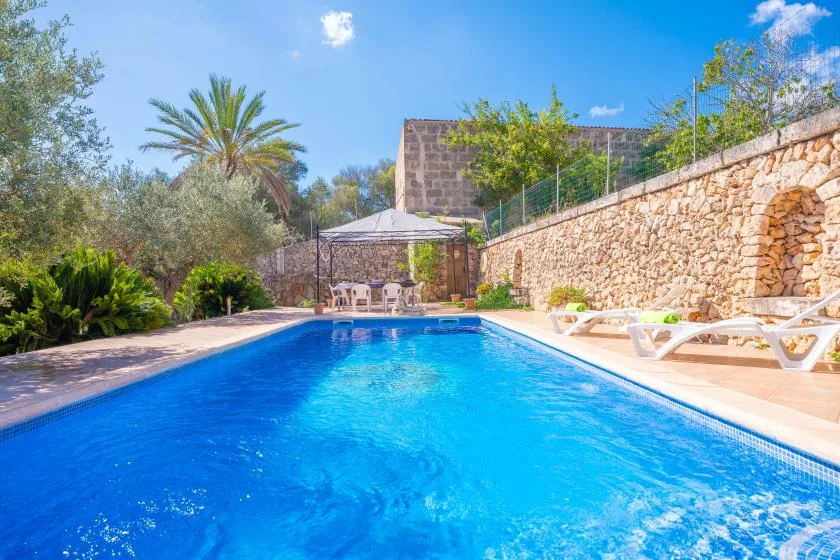 An outdoor swimming pool sits beside a stone wall and garden.