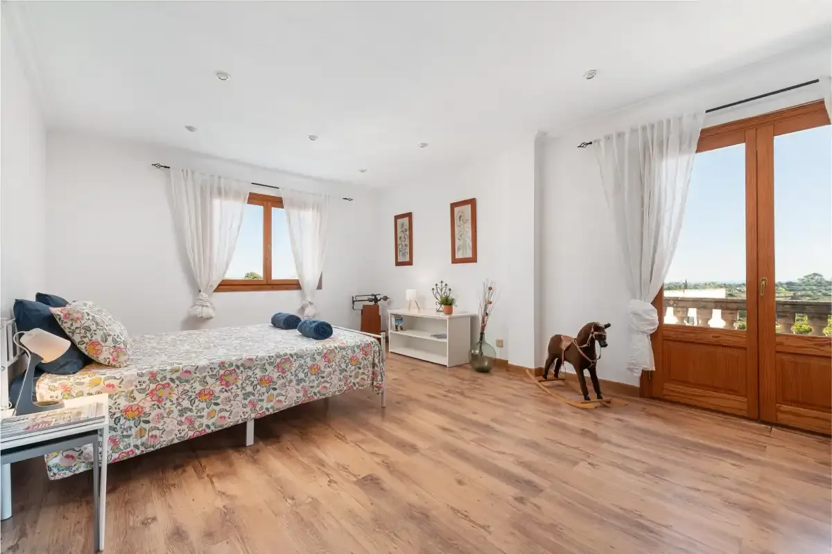 A bright bedroom with a floral bedspread and wooden doors opening onto a balcony.
