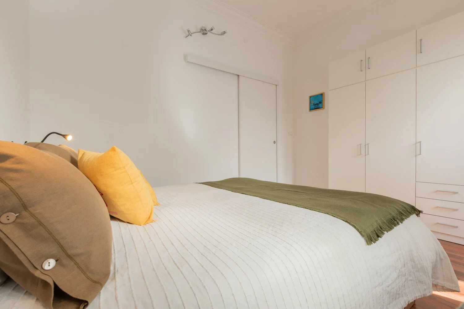 A bedroom with a neatly made bed and built-in cabinets along the wall.