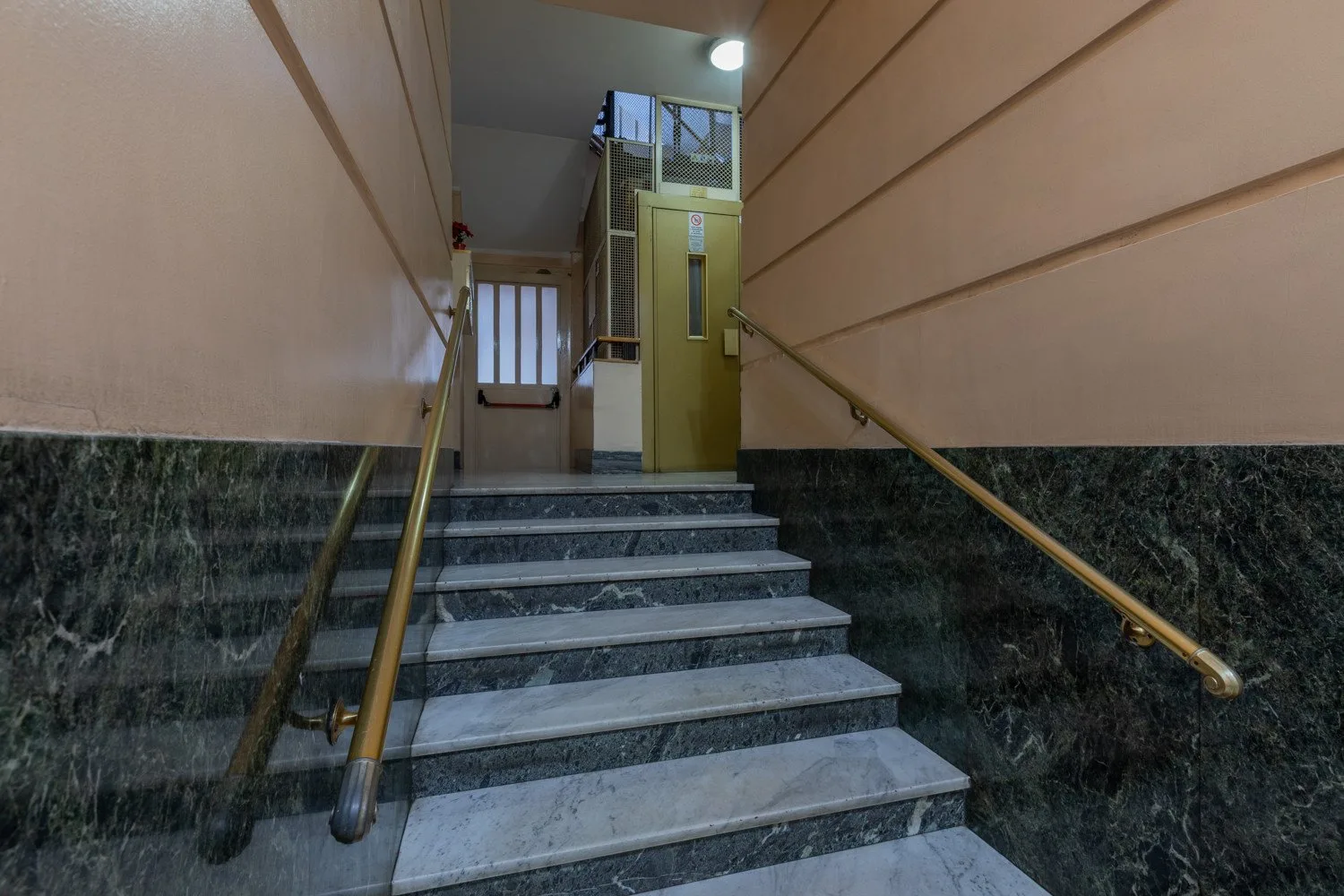 A stairwell with stone steps leads to a landing and a closed door.