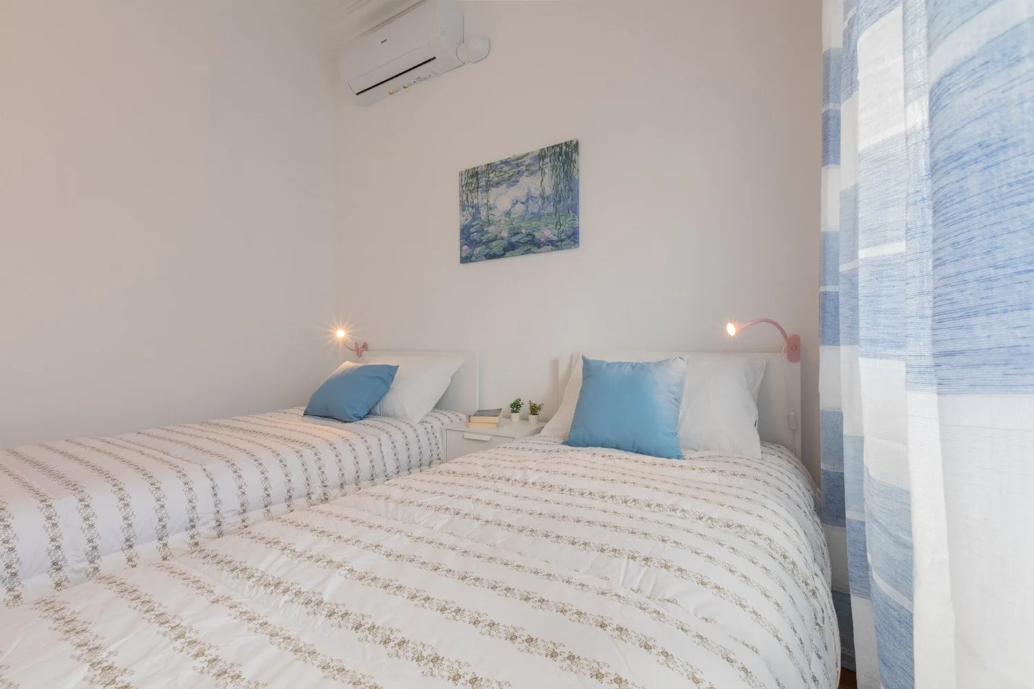 A bedroom with two beds, blue pillows, and a window with sheer curtains.