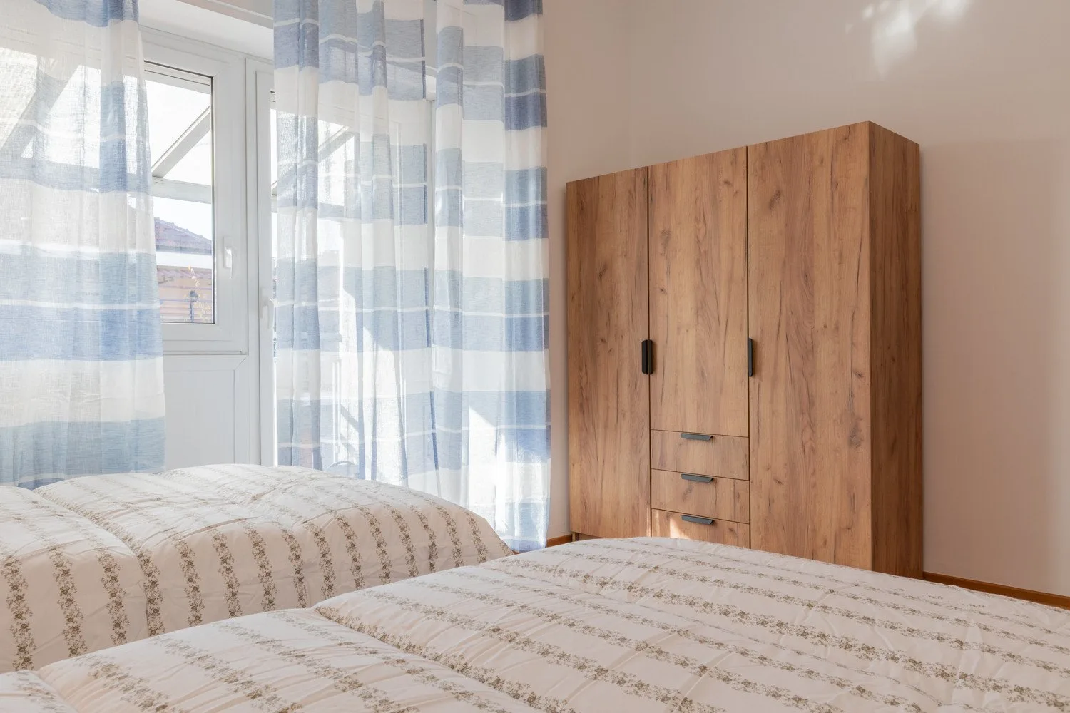 A bedroom with two beds, a wooden wardrobe, and striped curtains.