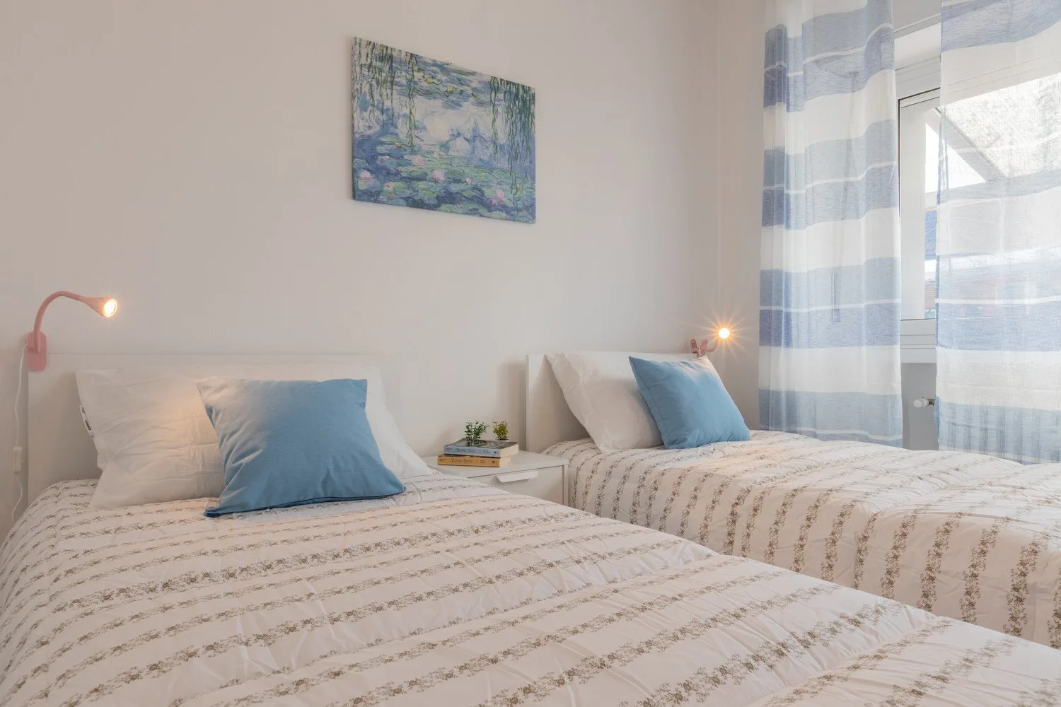 A bedroom with two beds, blue pillows, and striped curtains beside the window.
