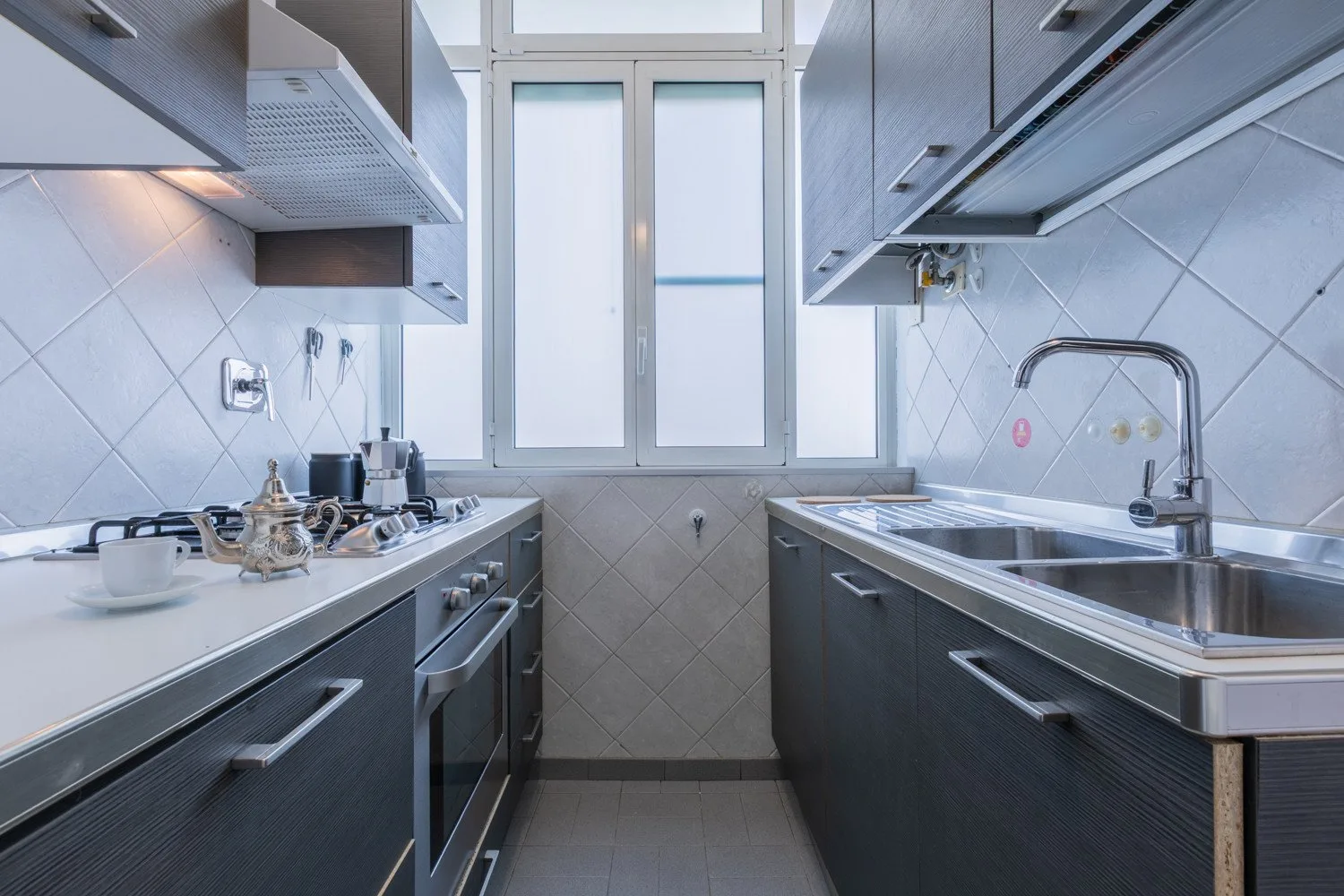 A narrow kitchen with counters and a sink beneath a bright window.