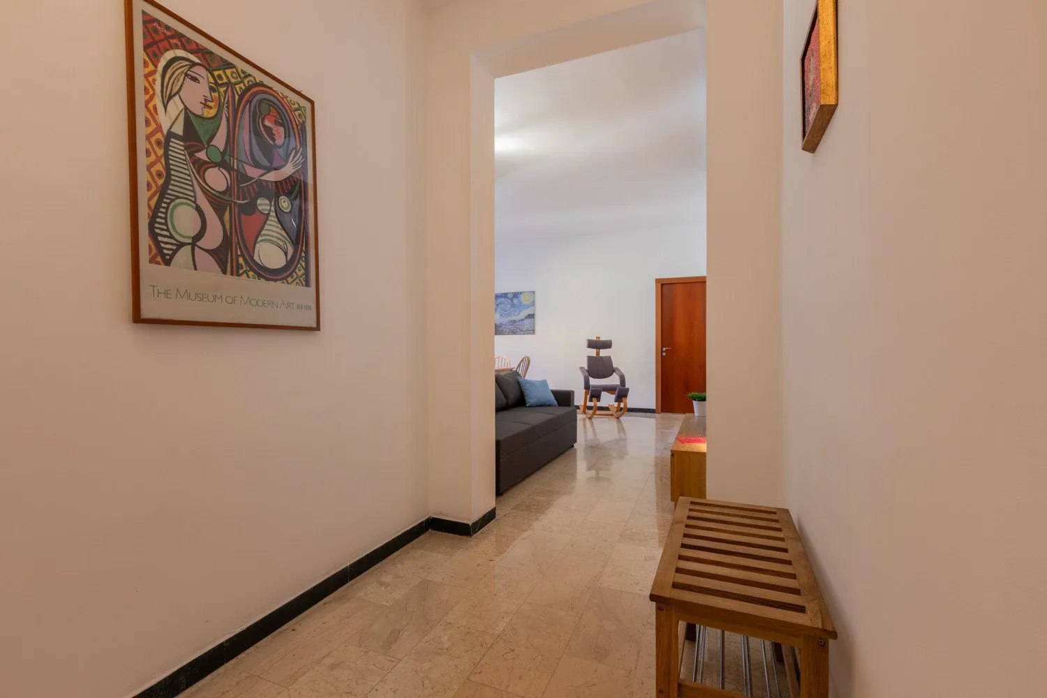A hallway opens into a living area, with wall art and a wooden bench.