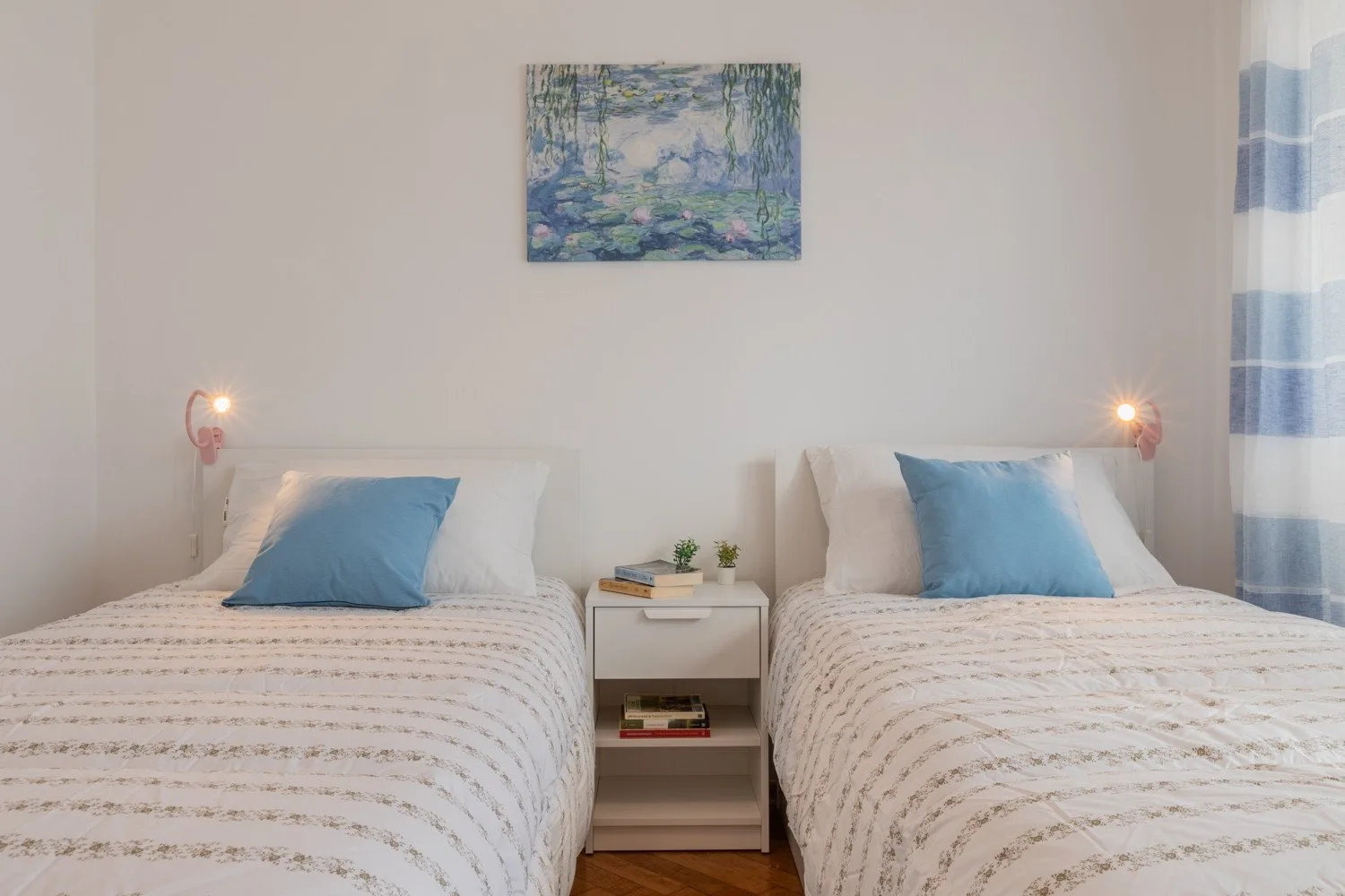 A bedroom with two beds, a small nightstand, and a painting on the wall.
