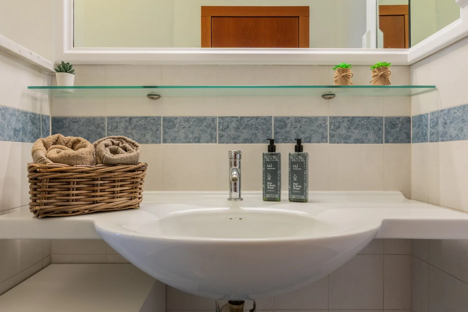 A bathroom vanity with a wide mirror, glass shelf, and basin.