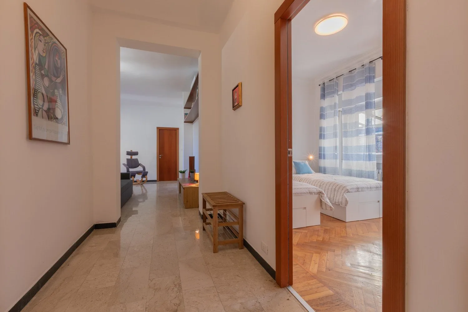 A hallway opens into a bedroom with a bed beside a curtained window.