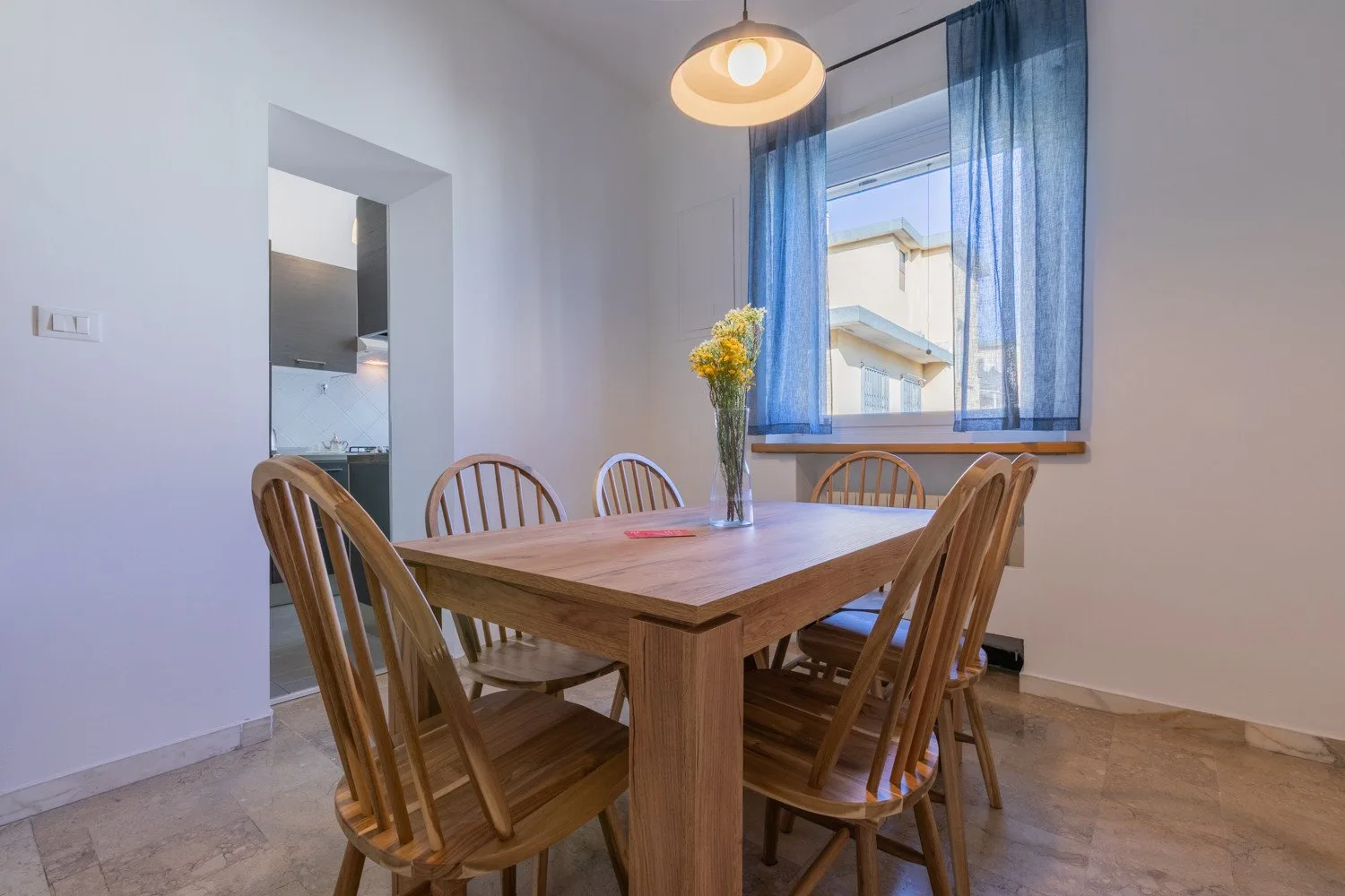 A dining area with a wooden table and chairs beside a window with blue curtains.