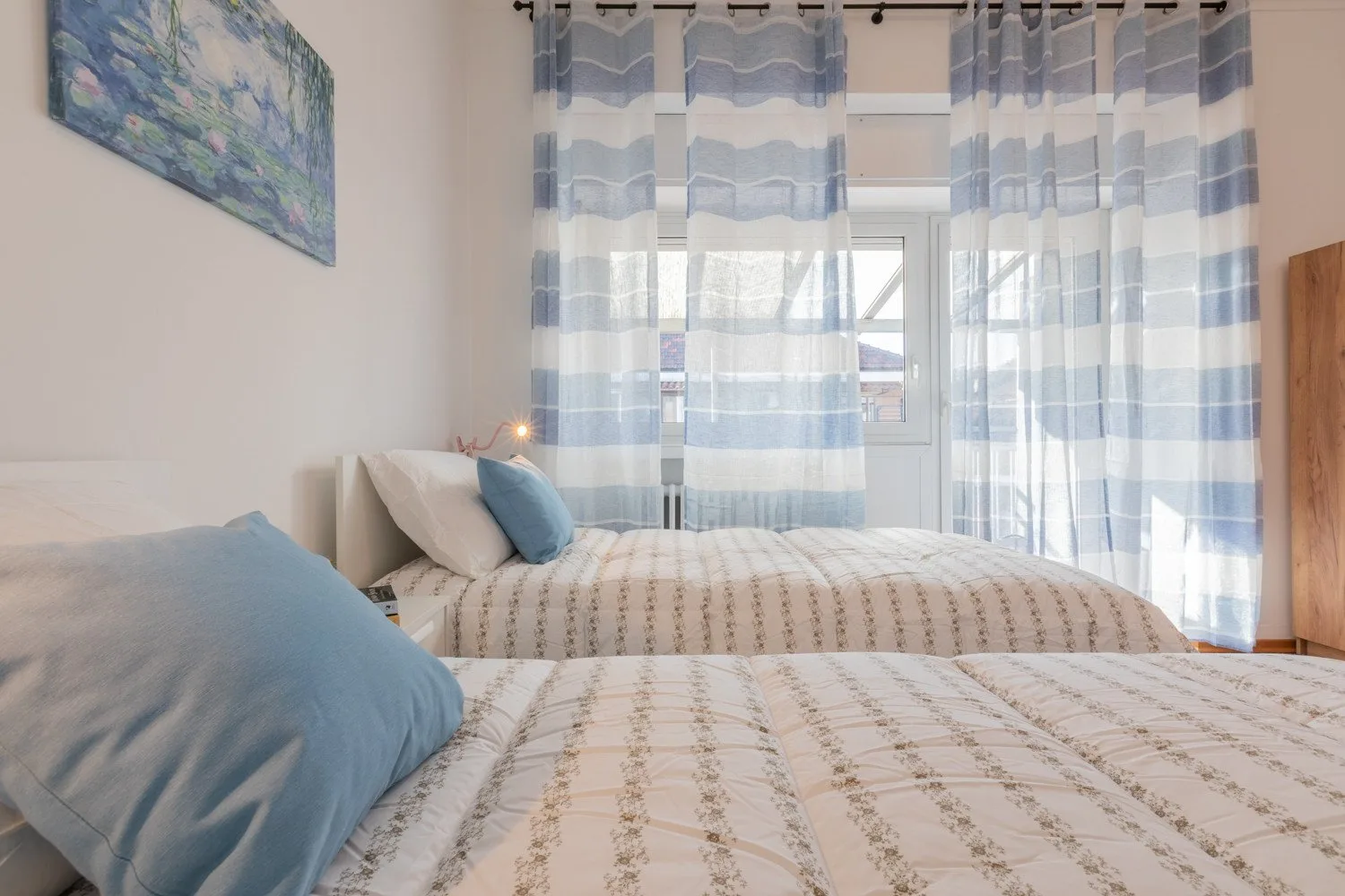 A bedroom with patterned bedding, blue pillows, and sheer striped curtains.