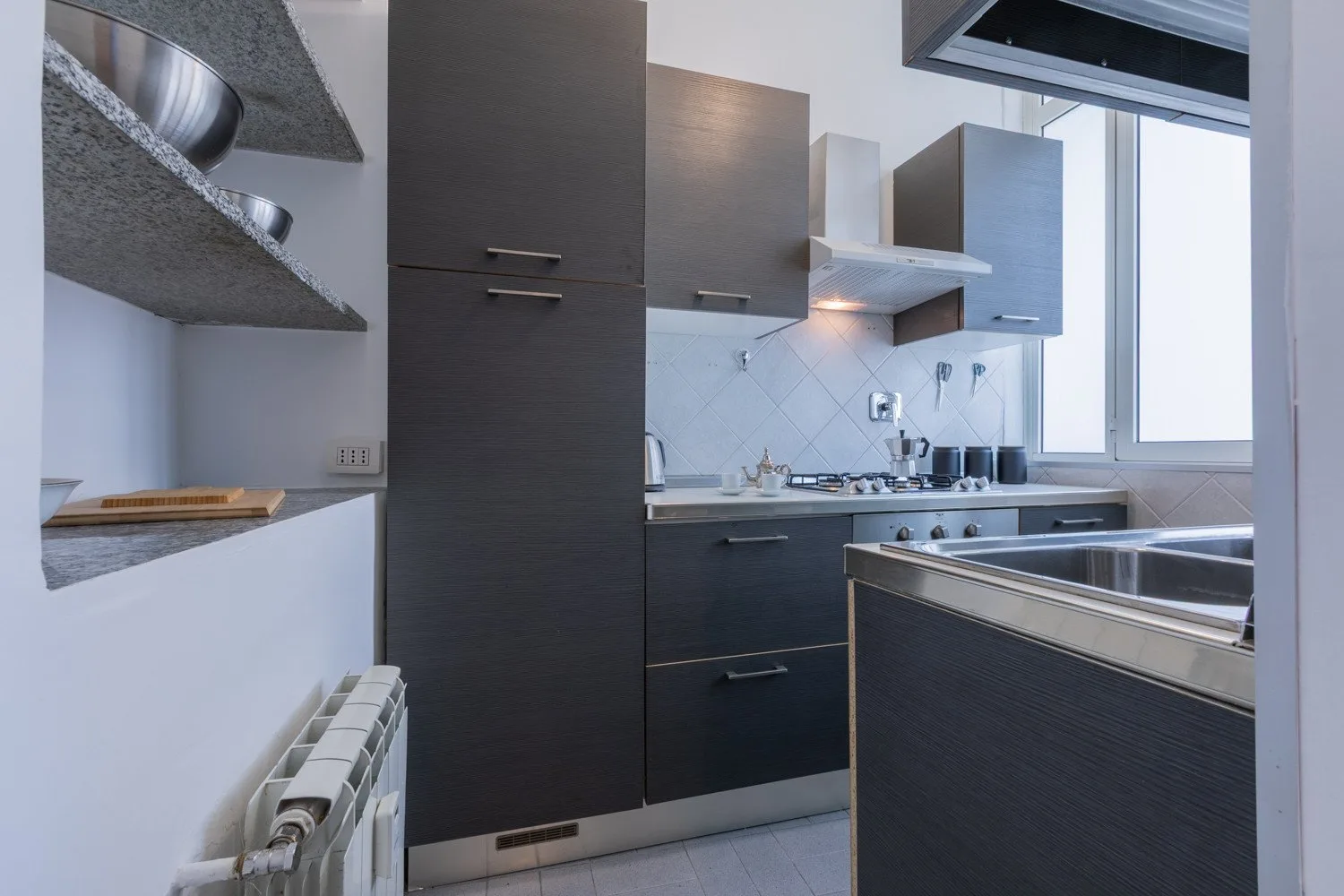 A modern kitchen with dark cabinets, a countertop, and a large window.