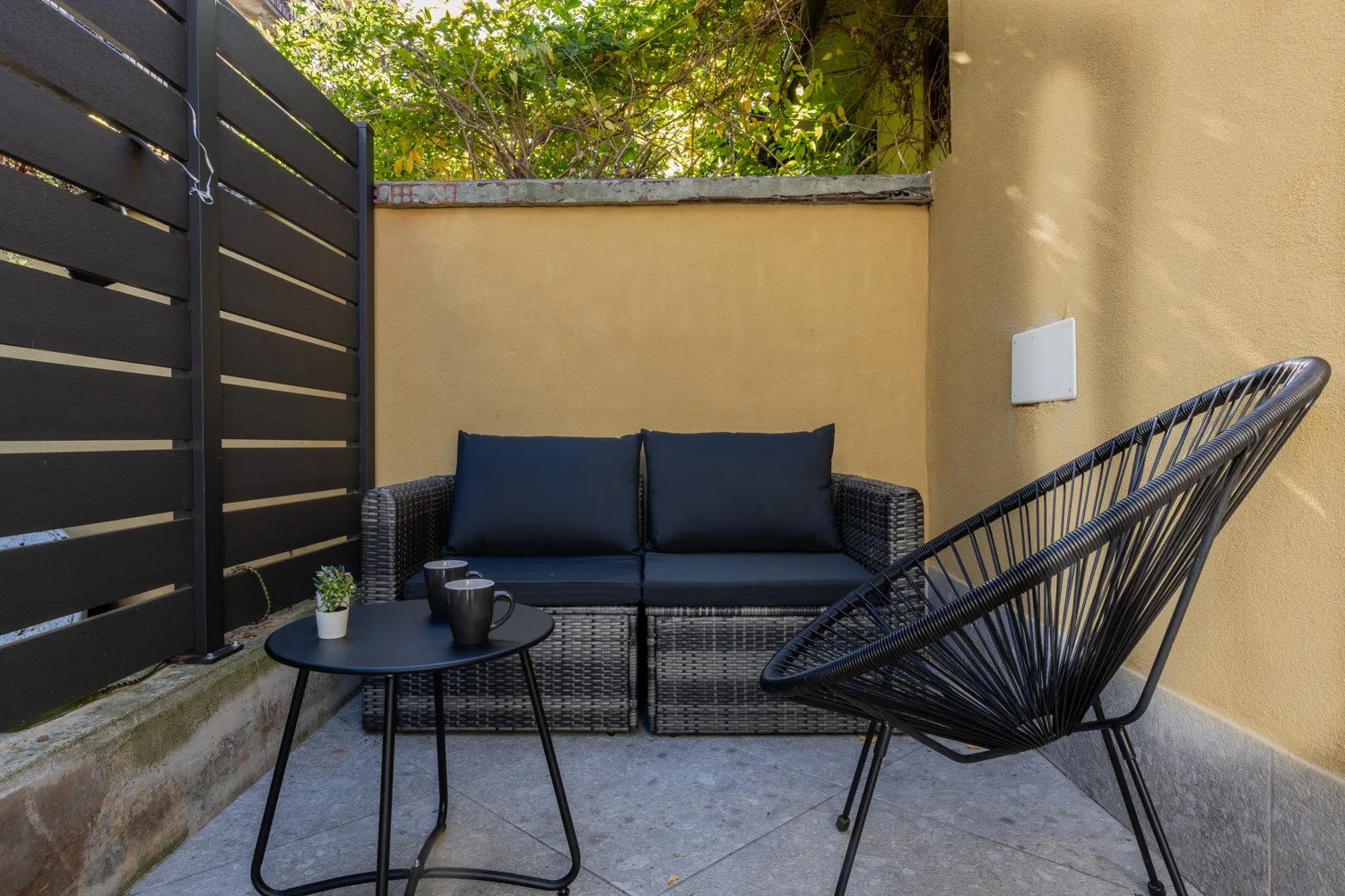 An outdoor patio seating area with a small table and leafy greenery above the wall.