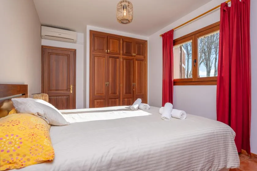 Un dormitorio con una cama grande, armarios de madera y una ventana con cortinas rojas.