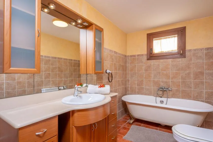 Un baño con azulejos cuenta con un largo tocador, una bañera y una ventana pequeña.