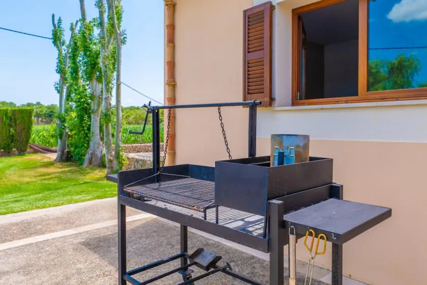 Una parrilla exterior está junto a la pared y una ventana de la casa.