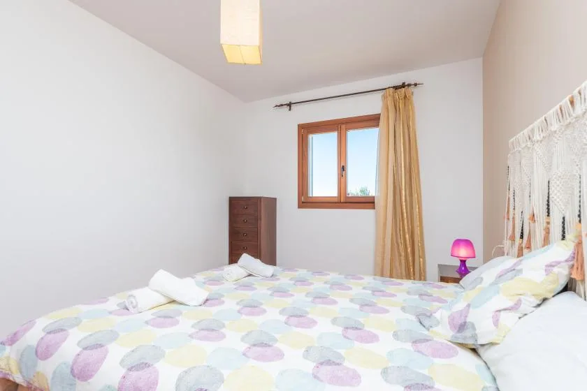 Un dormitorio con una cama cubierta de ropa de cama estampada en tonos pastel y una ventana.