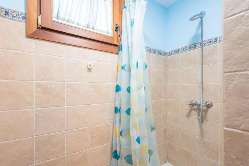 Zona de ducha con azulejos, una cortina estampada y un cabezal de ducha en la pared.
