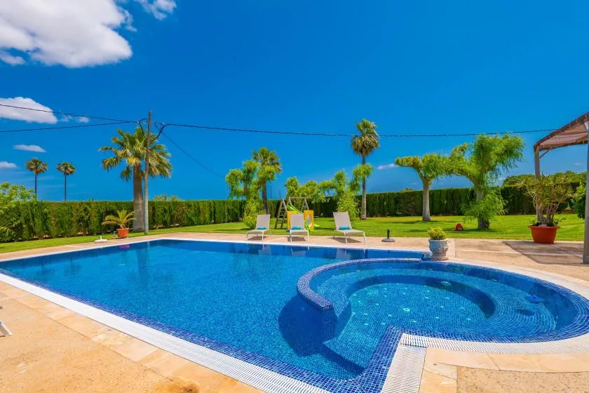 Una piscina en el patio con una sección poco profunda curva, tumbonas y palmeras.
