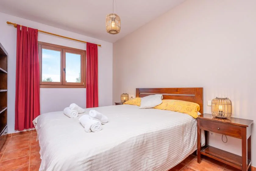 Un dormitorio con una cama, cortinas rojas y una ventana con vistas a la vegetación.