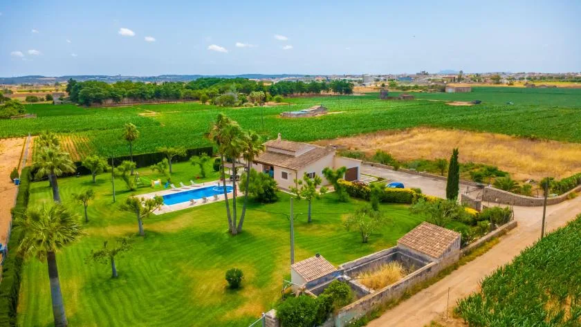 Una propiedad rural está rodeada de césped verde, una piscina y campos.