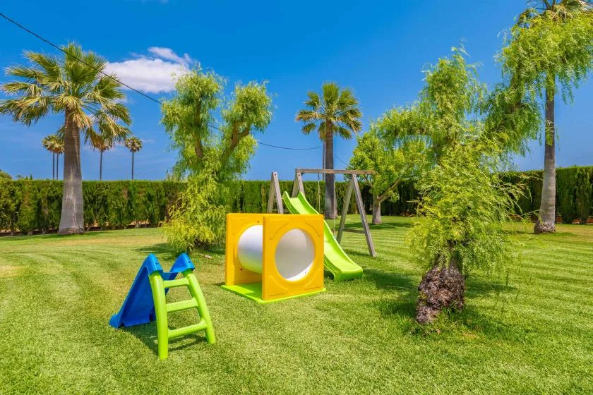 Una zona de juegos al aire libre con césped, una estructura colorida y palmeras.