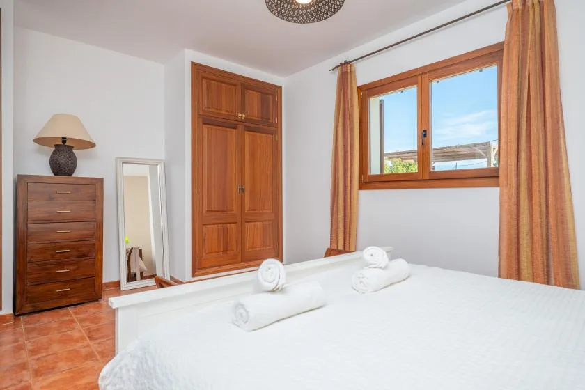 Un dormitorio luminoso con cama blanca, armario de madera y ventana con cortinas.