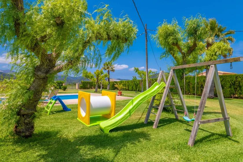 Un parque infantil al aire libre con un tobogán verde y columpios de madera sobre el césped.