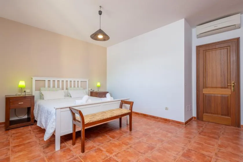 Un dormitorio con cama doble, mesitas de noche y un banco de madera.