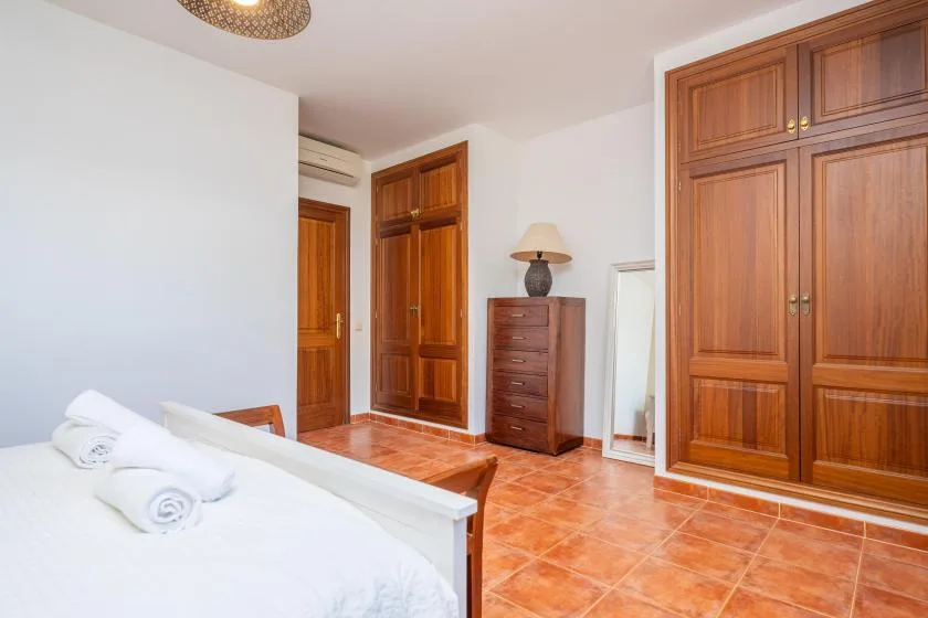 Un dormitorio con una cama blanca, armarios de madera y suelo de baldosas color terracota.